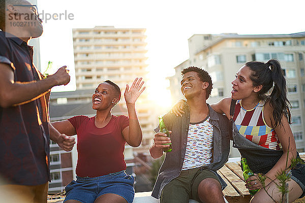 Glückliche junge Freunde trinken Bier und hängen auf dem sonnigen Dach der Stadt herum