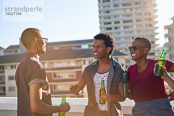 Junge Freunde unterhalten sich und trinken Bier auf dem sonnigen Balkon auf dem Dach der Stadt