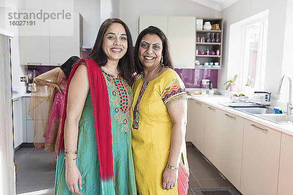 Porträt glücklicher indischer Schwestern in traditionellen Saris in der Küche