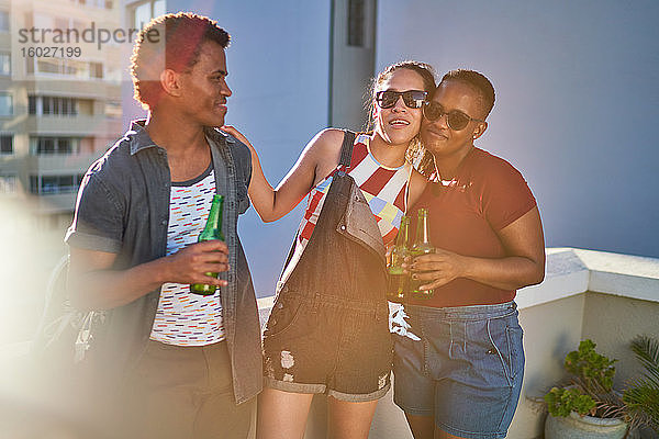 Glückliche junge Freunde trinken Bier auf dem sonnigen Stadtbalkon