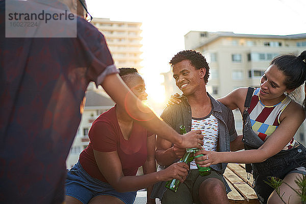 Glückliche junge Freunde trinken Bier auf dem sonnigen städtischen Dachbalkon