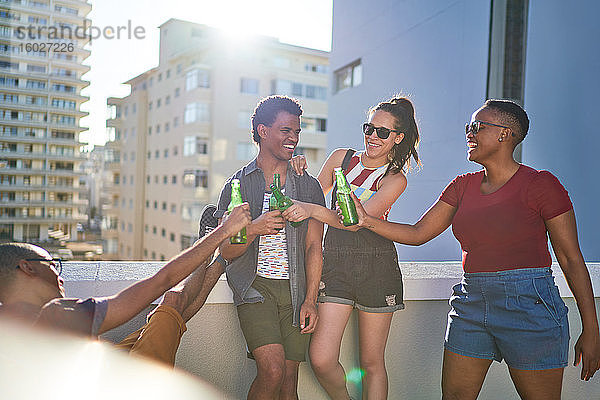 Glückliche junge Freunde stoßen auf Bierflaschen auf dem sonnigen Stadtbalkon an