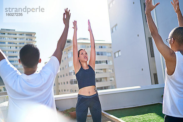 Junge Freunde praktizieren Yoga auf dem sonnigen städtischen Dachbalkon