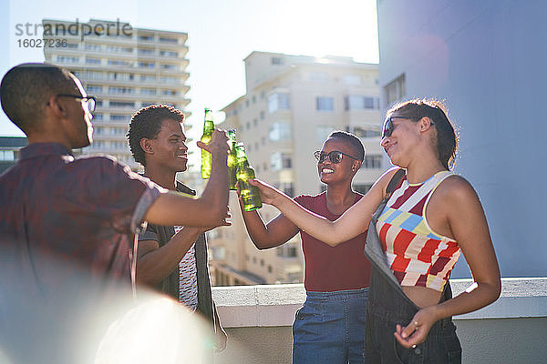 Glückliche junge Freunde trinken Bier auf dem sonnigen städtischen Dach