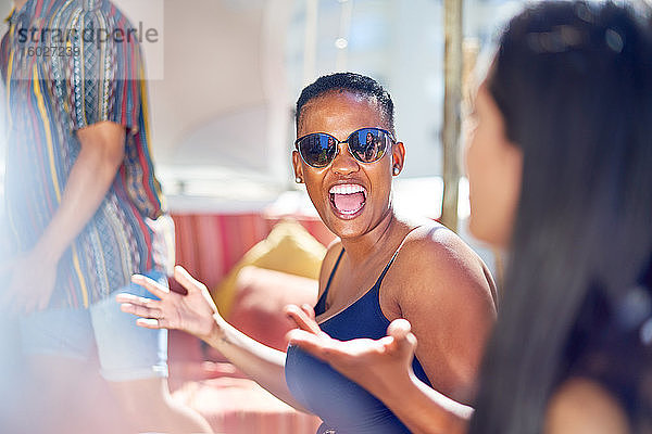 Glückliche junge Frau lacht mit Freunden auf sonniger Terrasse