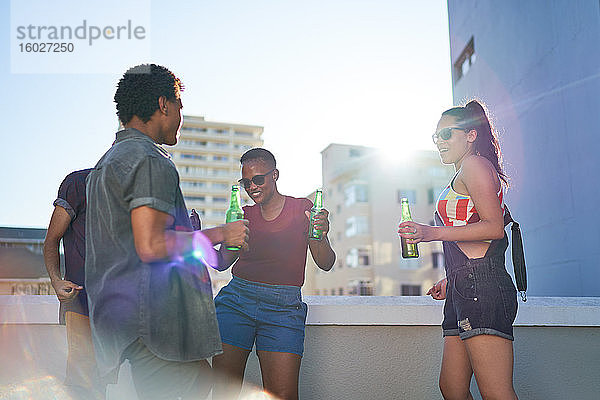 Junge Freunde tanzen und trinken Bier auf dem sonnigen städtischen Dachbalkon