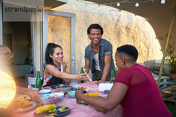 Glückliche junge Freunde mit Smartphone beim Mittagessen am Terrassentisch