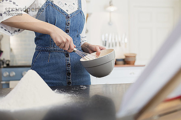 Teenagerin mit Schneebesen und Schüssel beim Backen in der Küche