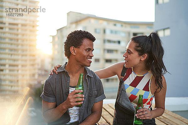 Glückliches junges Paar trinkt Bier auf sonnigem städtischen Dachbalkon