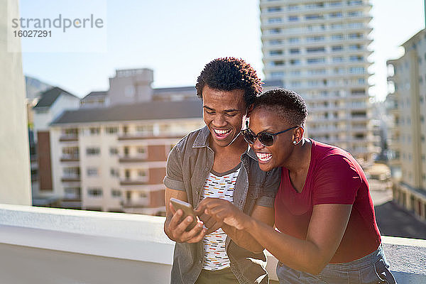 Glückliches junges Paar nutzt Smartphone auf sonnigem städtischen Dachbalkon