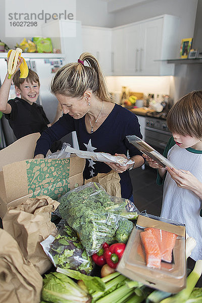 Frau und Söhne entladen frische Produkte aus der Kiste in der Küche