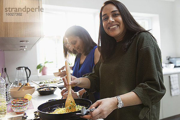 Porträt einer glücklichen indischen Frau  die in der Küche am Herd kocht