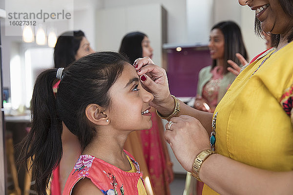 Indische Mutter legt der lächelnden Tochter ein Band auf die Stirn
