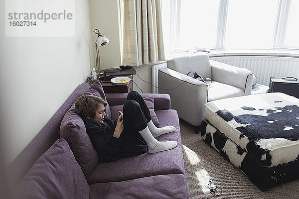 Junge benutzt Smartphone auf Wohnzimmer-Sofa