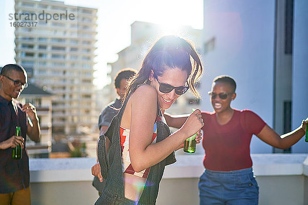 Glückliche junge Freunde tanzen und trinken Bier auf dem sonnigen Dach der Stadt