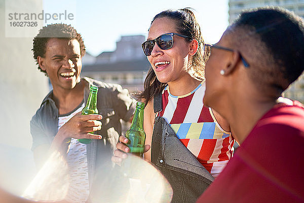 Glückliche junge Freunde trinken Bier auf dem sonnigen Balkon