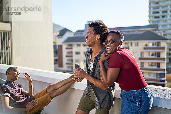 Glückliches junges Paar lacht und umarmt sich auf sonnigem Stadtbalkon