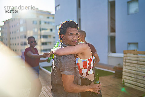 Porträt eines jungen Paares  das sich umarmt und Bier auf dem Dach einer Stadt trinkt