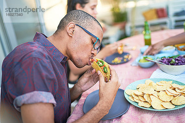 Junger Mann isst Taco am Terrassentisch