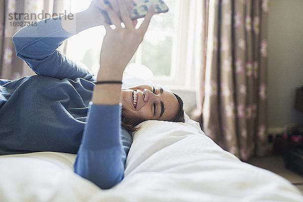 Glückliches Teenager-Mädchen benutzt Smartphone im Bett