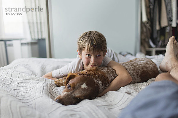 Süßer Junge kuschelt mit Hund auf dem Bett