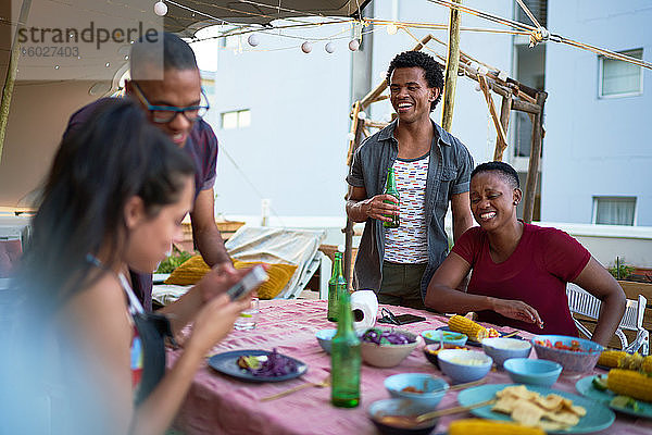 Glückliche junge Freunde beim Abendessen auf dem Dachbalkon