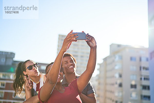 Junge Freunde beim Selbstfahren mit dem Smartphone auf dem sonnigen Stadtdach