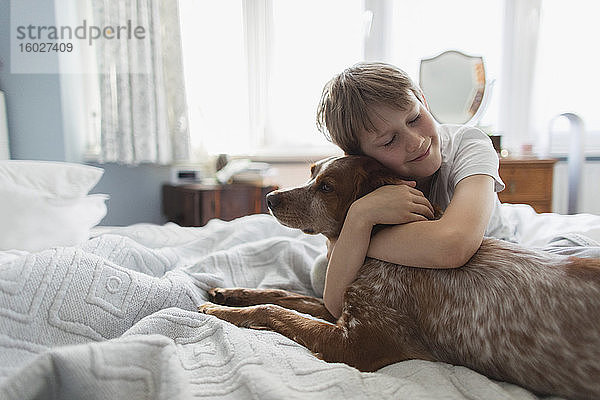 Süßer Junge umarmt Hund auf dem Bett