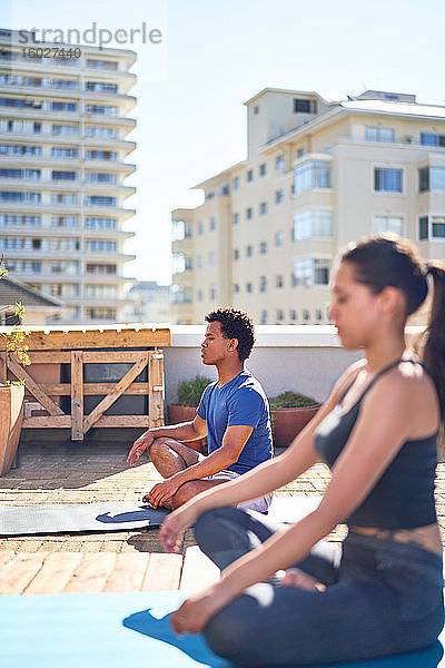 Junger Mann und Frau praktizieren Yoga auf einem sonnigen städtischen Dach