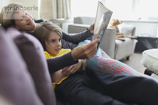 Glückliche Mutter und Sohn lesen Buch auf Wohnzimmersofa