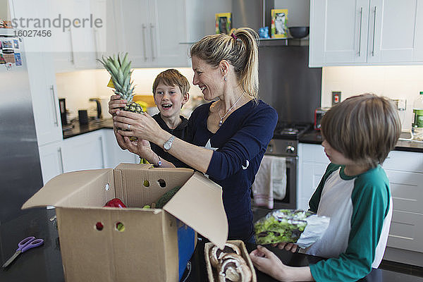 Glückliche Mutter und Söhne entladen frische Produkte aus dem Karton in der Küche