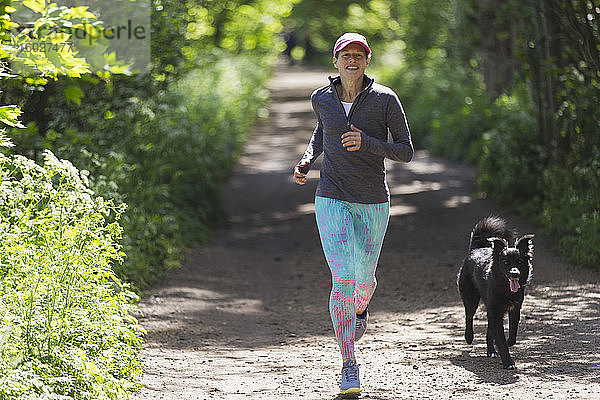 Frau joggt mit Hund auf sonniger Strecke