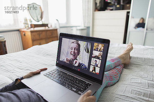 Frau mit Laptop im Video-Chat mit Freunden im Bett