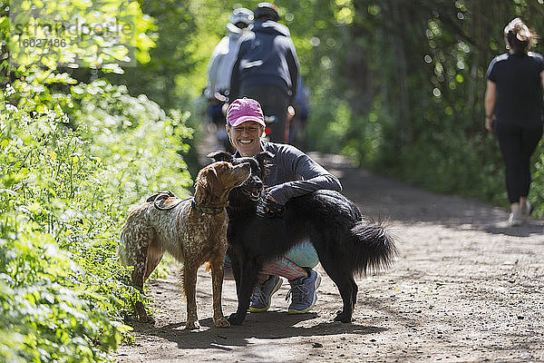 Glückliche Frau wandert mit Hunden auf sonnigem Pfad