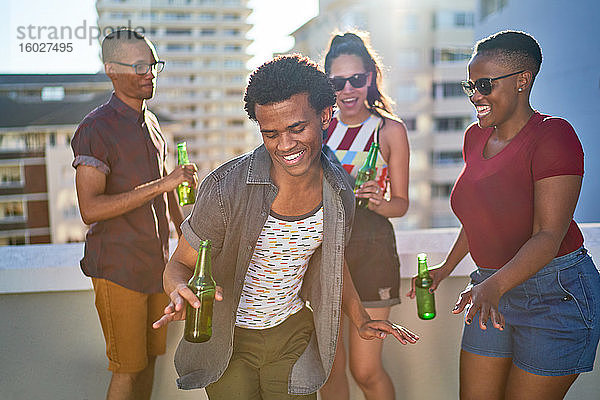 Sorglose junge Freunde trinken Bier auf dem sonnigen städtischen Dach