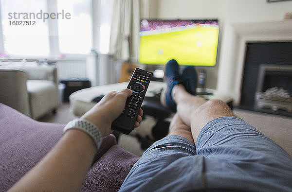 POV-Mann mit Fernbedienung sieht Fußballspiel auf Wohnzimmer-Sofa