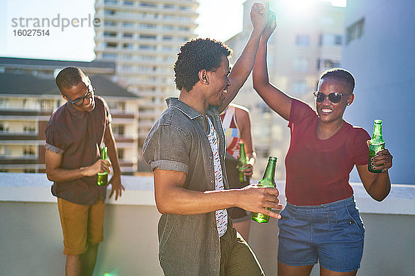 Glückliche junge Freunde tanzen und trinken Bier auf dem sonnigen Dach der Stadt