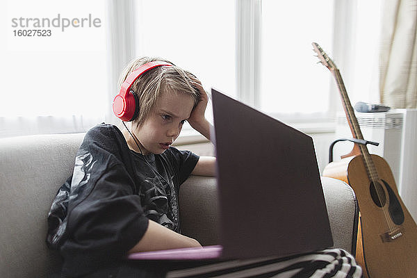 Junge mit Kopfhörer und Laptop auf Wohnzimmersofa