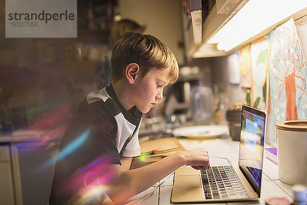 Fokussierter Junge macht Hausaufgaben am Laptop in der Küche