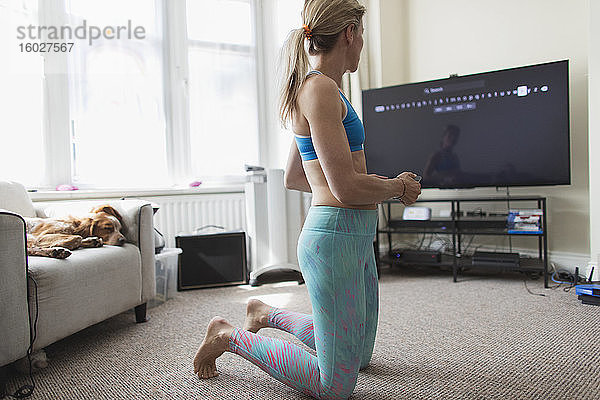 Frau praktiziert Online-Yoga am Fernseher im Wohnzimmer