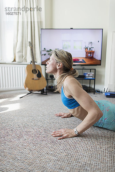 Frau praktiziert Yoga am Fernseher im Wohnzimmer