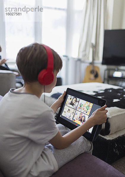 Junge mit Kopfhörern und digitalem Tablet Heimunterricht auf dem Sofa