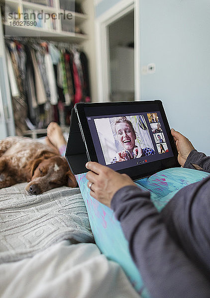 Frau mit digitalem Tablet Video-Chat mit Freunden im Bett mit Hund