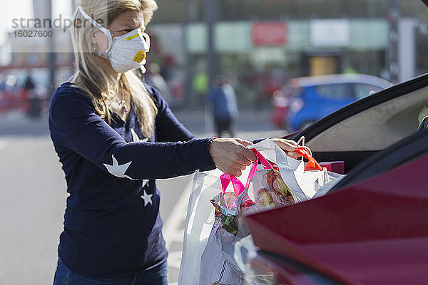 Frau mit Gesichtsmaske lädt Lebensmittel ins Auto