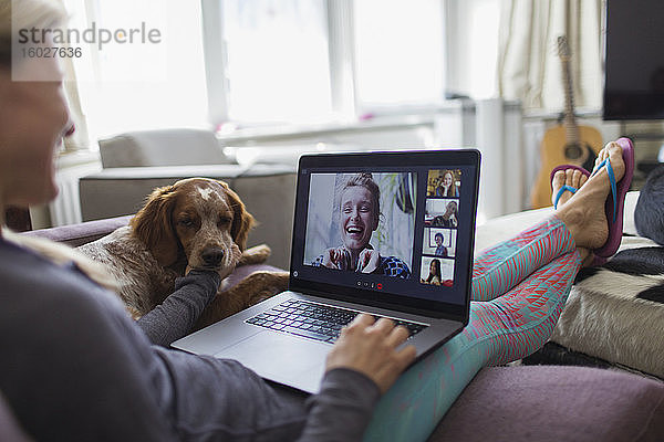 Frau mit Laptop im Video-Chat mit Freunden auf dem Sofa mit Hund