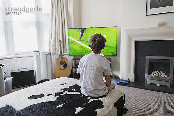 Junge schaut im Wohnzimmer ein Fußballspiel im Fernsehen