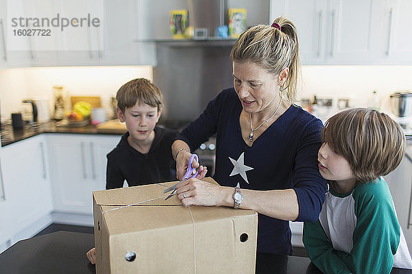 Mutter und Söhne öffnen Paket in der Küche