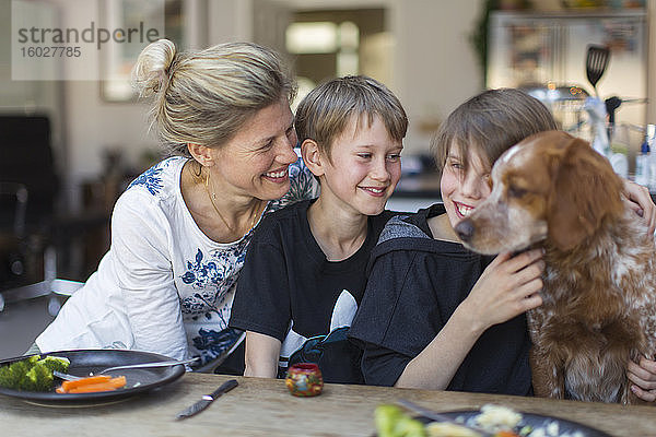 Glückliche Mutter und Söhne mit Hund am Esstisch