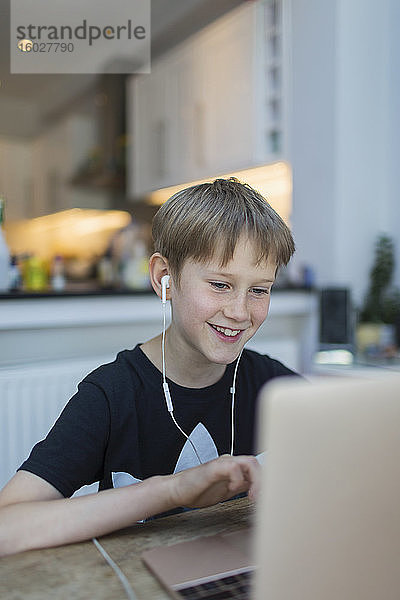 Lächelnder Junge mit Kopfhörern beim Heimunterricht am Laptop