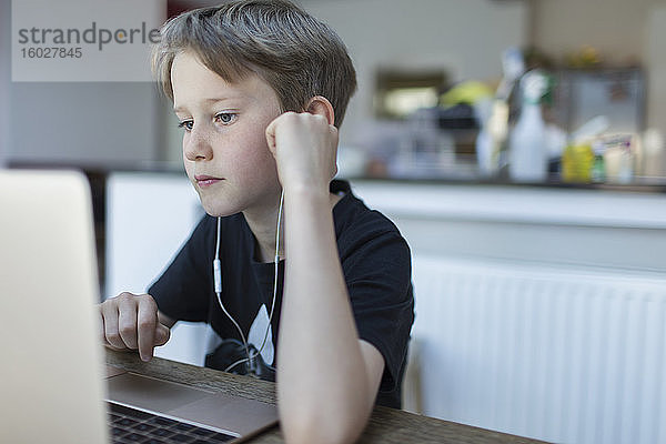 Fokussierter Junge mit Kopfhörern beim Heimunterricht am Laptop